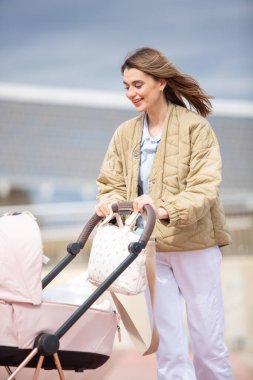 Genç anne, bebek arabasını dışarı iterken gülümseyerek, dışarıda huzurlu bir gezintiden hoşlanıyor.