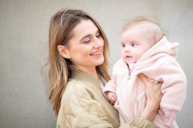 Pembe bir tulum içinde bebeğini kucağında tutan, sıcak ve sevgi dolu bir anı paylaşan bir anne portresi..