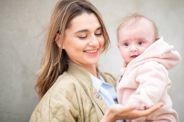 Gülümseyen anne bebeğini sevgiyle tutuyor. Pembe bir post giymiş.