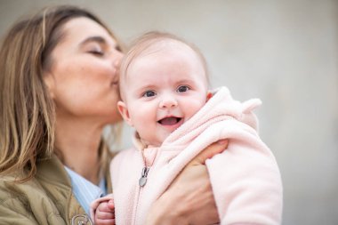 Pembe bir postun içindeki gülümseyen bebek, onu nazikçe başından öpen annesi tarafından tutulur.
