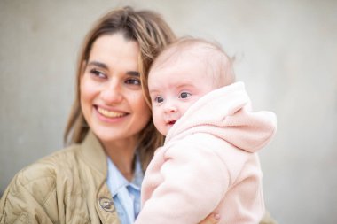 Mutlu bir annenin portresi bebeğini kucaklıyor, hem gülümsüyor hem de hassas bir anı paylaşıyor.