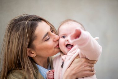 Neşeli bebek, annesi tarafından öpülürken uzanıyor, sıcaklık ve sevgiyle dolu şefkatli ve neşeli bir anı yakalıyor..