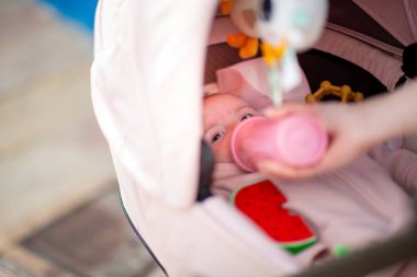 Bebek, pembe bir şişeyle beslenirken bebek arabasında rahat bir şekilde yatıyor.