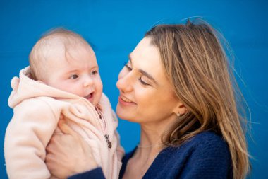 Anne pembe ceketli bebeğe gülümsüyor.