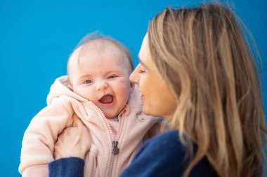 Anne gülümseyen bebeğini mavi bir arkaplanda tutuyor.