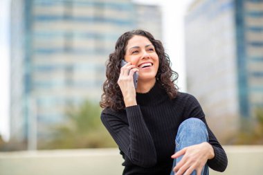 Şehirde telefonda konuşurken gülen genç bir kadın.