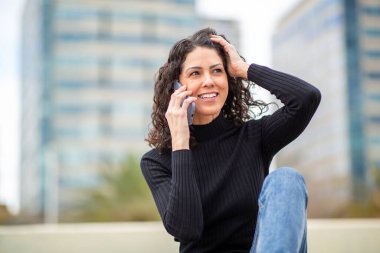 Şehir merkezinde telefonla konuşurken gülümseyen bir kadın..