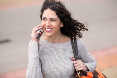 Gülümseyen kadın cep telefonuyla yürüyor ve konuşuyor.