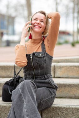 Dışarıda cep telefonuyla konuşurken gülümseyen neşeli kadın.