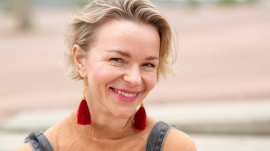 Yakın plan neşeli, orta yaşlı, kısa sarı saçlı bir kadın.