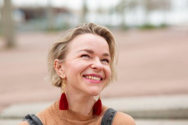 Gülümseyen orta yaşlı sarışın bir kadının yakın portresi.