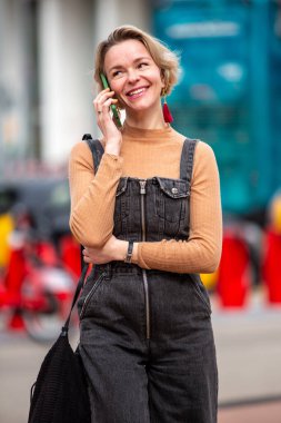 Gülümseyen orta yaşlı kadın şehirde telefonla konuşuyor.