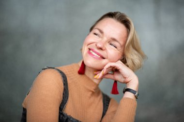 Kadın düşünceli ama neşeli bir pozda oturur, başını eline koyar ve sıcak bir gülümsemeyle yan tarafa bakar.