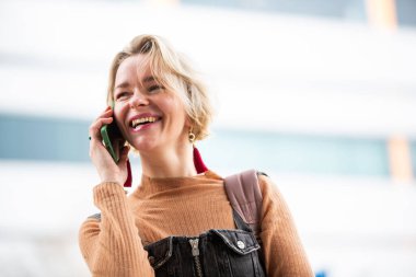 Kısa sarı saçlı neşeli kadın cep telefonuyla konuşuyor.