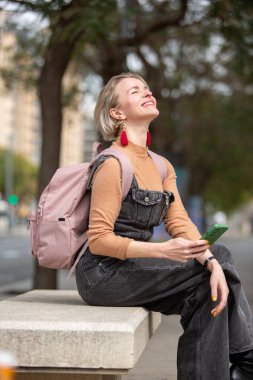 Kadın, şehir merkezinde bir bankta otururken, parlak bir gülümsemeyle, hafif bir anın tadını çıkarır.