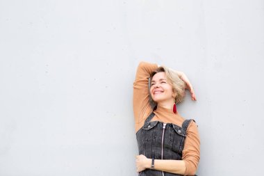 Tulumlu gülümseyen sarışın kadın beyaz duvara poz veriyor.