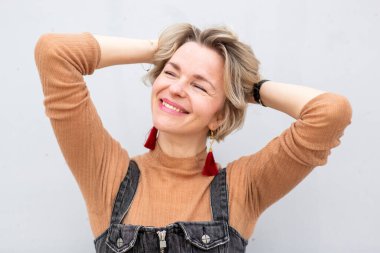 Sarışın kadın samimi bir şekilde poz veriyor, elleri saçında.