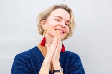 Kısa sarı saçlı, kırmızı püsküllü, gülümseyen kadın ve neşeli bir poz içinde ellerini sıktı.