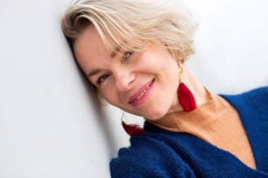 Gülümseyen, kısa sarı saçlı, başını yavaşça duvara yaslayan bir kadının yakın çekimi.