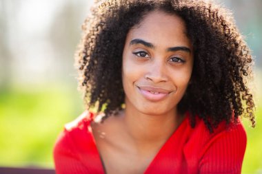 Güzel siyah kadın sıcak bir şekilde gülümsüyor, doğal kıvırcık saçlar gün ışığında parlıyor..