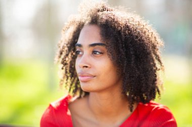 Kıvırcık saçlı, güneş ışığıyla özelliklerini vurgulayan siyah bir kadının profili..