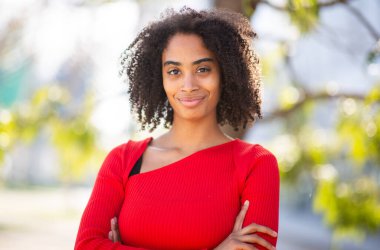 Dışarıda duran genç bir kadın, kollarını kavuşturmuş kendine güvenen bir ifade.