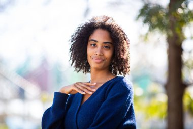 Mavi bir kazak giyen bir kadının portresi, yakasına yakın bir el pozu, sakin bir ifade..