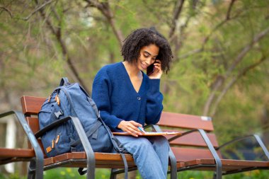 Genç Afrikalı kadın dışarıda çalışıyor ve telefonla konuşuyor.