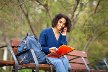 Dışarıda çalışırken telefonla konuşan gülümseyen bir öğrenci.