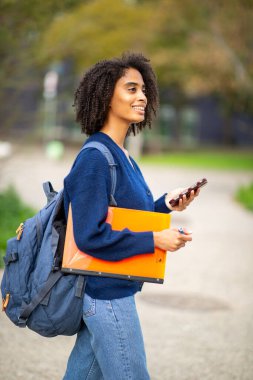 Telefon ve klasörle yürüyen öğrencinin yan görünümü
