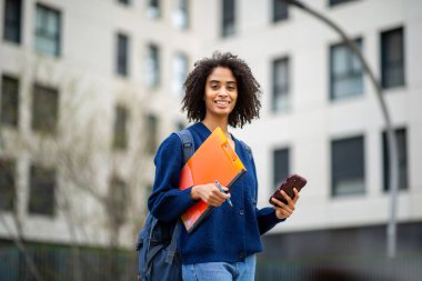 Sırt çantalı öğrenci telefon ve klasörü binanın yanında tutuyor.
