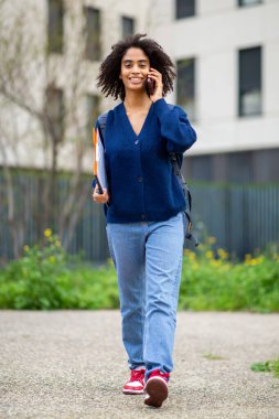 Dışarıda yürürken telefonla konuşan gülümseyen bir öğrenci.