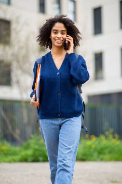 Sırt çantası ve klasörle yürüyen neşeli Afrikalı Amerikalı kadın.