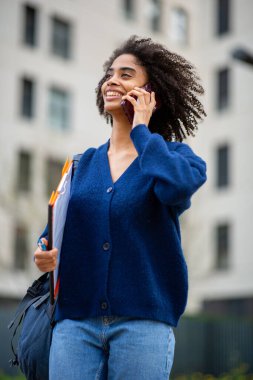 Dosyasıyla yürüyen ve telefonla konuşan mutlu genç bir kadın.