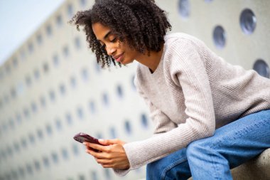 Kadın bankta otururken cep telefonu kullanıyor.