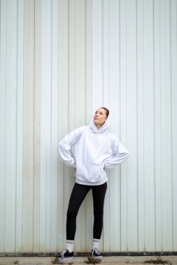 Beyaz duvarın yanında duran kendinden emin genç bir kadın.
