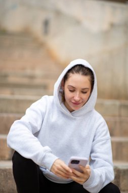 Dışarıda cep telefonuyla oturan genç bir kadın.