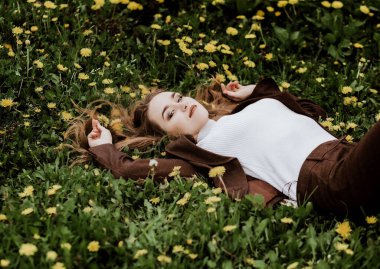 Yeşil çimenler ve sarı karahindibalar üzerinde kıvırcık saçlı kahverengi saçlı bir kızın portresi. Doğal saç bakımı. Doğal kozmetikler. Kadın bakımı. Hayalperest kız 20-25 yaşlarında. seçici odak