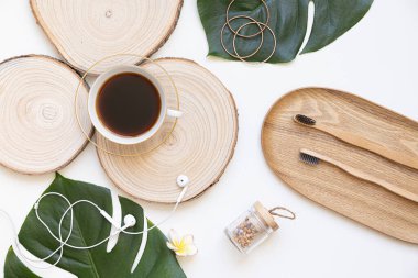 Bambu diş fırçası ve kahve beyaz arka planda fotokopi alanı olan bir masada. Tropikal yapraklarla bezenmiş düzlüğün stil bileşimi