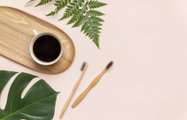 Bambu diş fırçası ve kahve pembe arka planda fotokopi alanı olan bir masada. Tropikal yapraklarla bezenmiş düzlüğün stil bileşimi