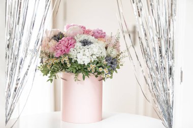 Pembe bir kutuda zarif bir buket gül, şakayık ve papatya. Işıkla dolu bir pencere tarafından güzelce düzenlenmiş ve yerleştirilmiş. Yüksek kalite fotoğraf. Doğum günleri ve düğünler için harika bir hediye.