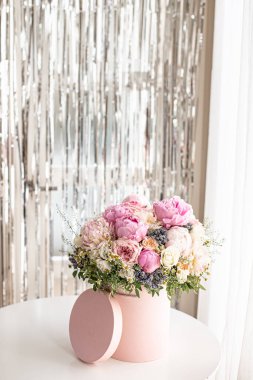 Pembe bir kutuda zarif bir buket gül, şakayık ve papatya. Işıkla dolu bir pencere tarafından güzelce düzenlenmiş ve yerleştirilmiş. Yüksek kalite fotoğraf. Doğum günleri ve düğünler için harika bir hediye.