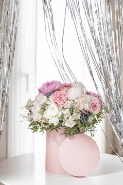 Pembe bir kutuda zarif bir buket gül, şakayık ve papatya. Işıkla dolu bir pencere tarafından güzelce düzenlenmiş ve yerleştirilmiş. Yüksek kalite fotoğraf. Doğum günleri ve düğünler için harika bir hediye.