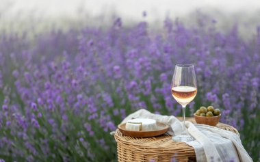 Lavanta tarlasında bir bardak beyaz şarap. Arka planda mor çiçekler