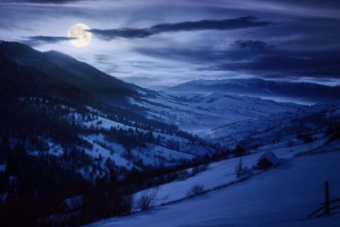 Geceleri dağ manzarası. Tepelerde karla kaplı ağaçlar. Gökyüzü dolunay ışığında parlayan bulutlarla