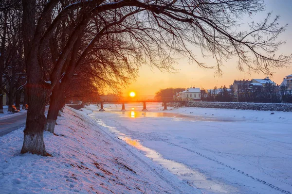 在乌日戈罗德的冬日日出 清晨美丽的城市景观 地平线上的太阳 冰封的河流上的桥 白雪覆盖的堤岸 — 图库照片
