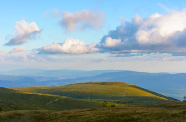 Karpatya dağlarında günbatımı manzarası. Akşam ışığında çimenli tepe. Pofuduk bulutlarla dolu muhteşem bir gökyüzünün altındaki uzak vadiye bak.