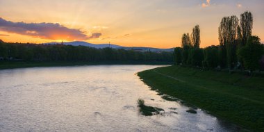 gorgeous sunrise on the waterfront of river uzh. beautiful urban scenery of uzhhorod downtown in spring. grassy embankment of longest linden alley in europe and kyiv embankment with chestnut trees