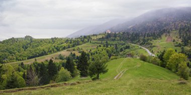 İlkbaharda kırsal dağ manzarası. Yuvarlanan tepelerdeki çimenli tepeler ve tarlalar. Bulutlu bir gökyüzünün altındaki uzak sırt