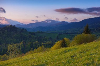 Kırsal dağ vadisinde gün batımı. Yuvarlanan tepeler ve dağ zirveleri çarpıcı bir zemin sağlar.